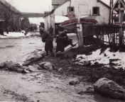 At a Belgian crossroads in the early hours of the battle of the Bulge, German soldiers strip boots and other equipment from three dead GIs. After U.S. troops captured this film, an Army censor redacted the road sign to Bllingen and other landmarks. from crossroads